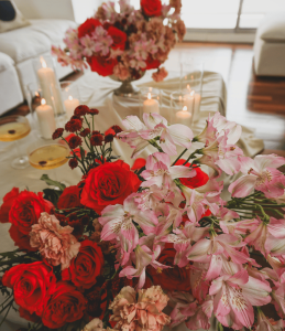 A close up of a floral arrangement including pink alstroemeria, roses, and carnations. Flowers are surrounded by candles in glass containers and a cream colored tablescape