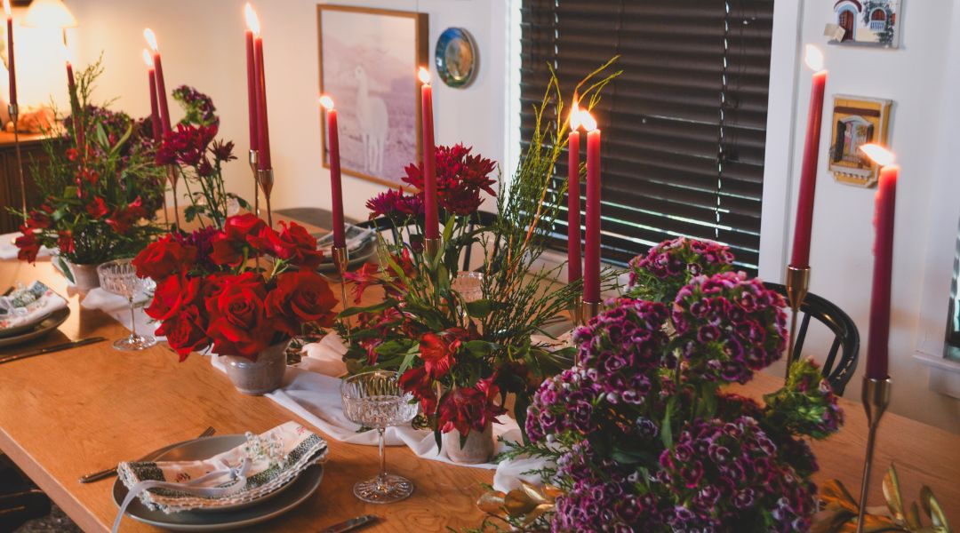 Holiday table decorated with red candles and floral arrangements featuring roses, alstroemeria, cushion flowers, and greens.