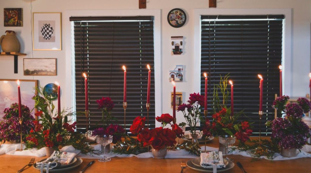 Long view of the holiday table showing a runner with multiple floral arrangements, red taper candles and pottery vases.
