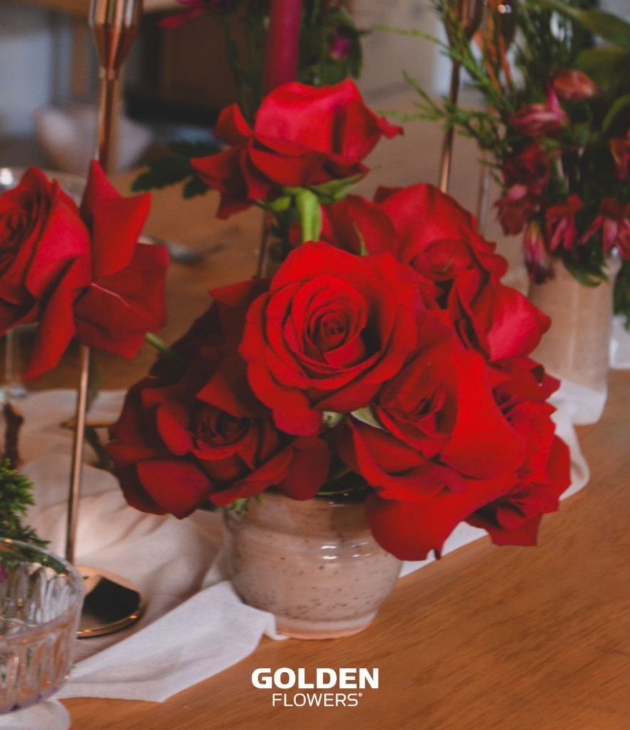 Red roses arranged in a ceramic vase as part of a holiday table setting.